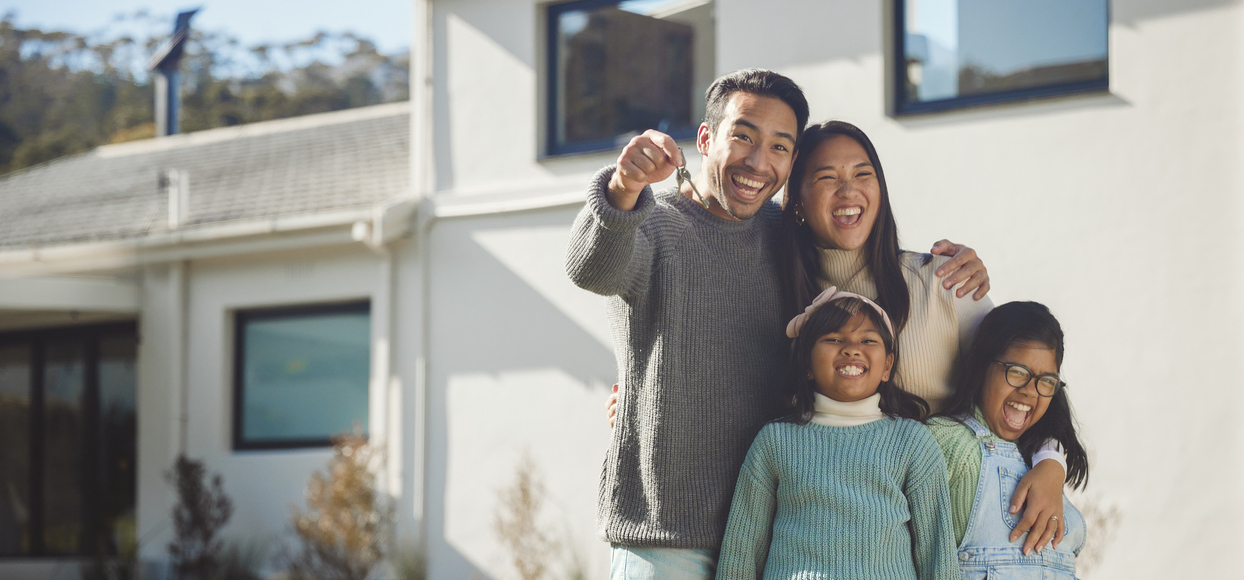 Family poses with keys in front of new home.