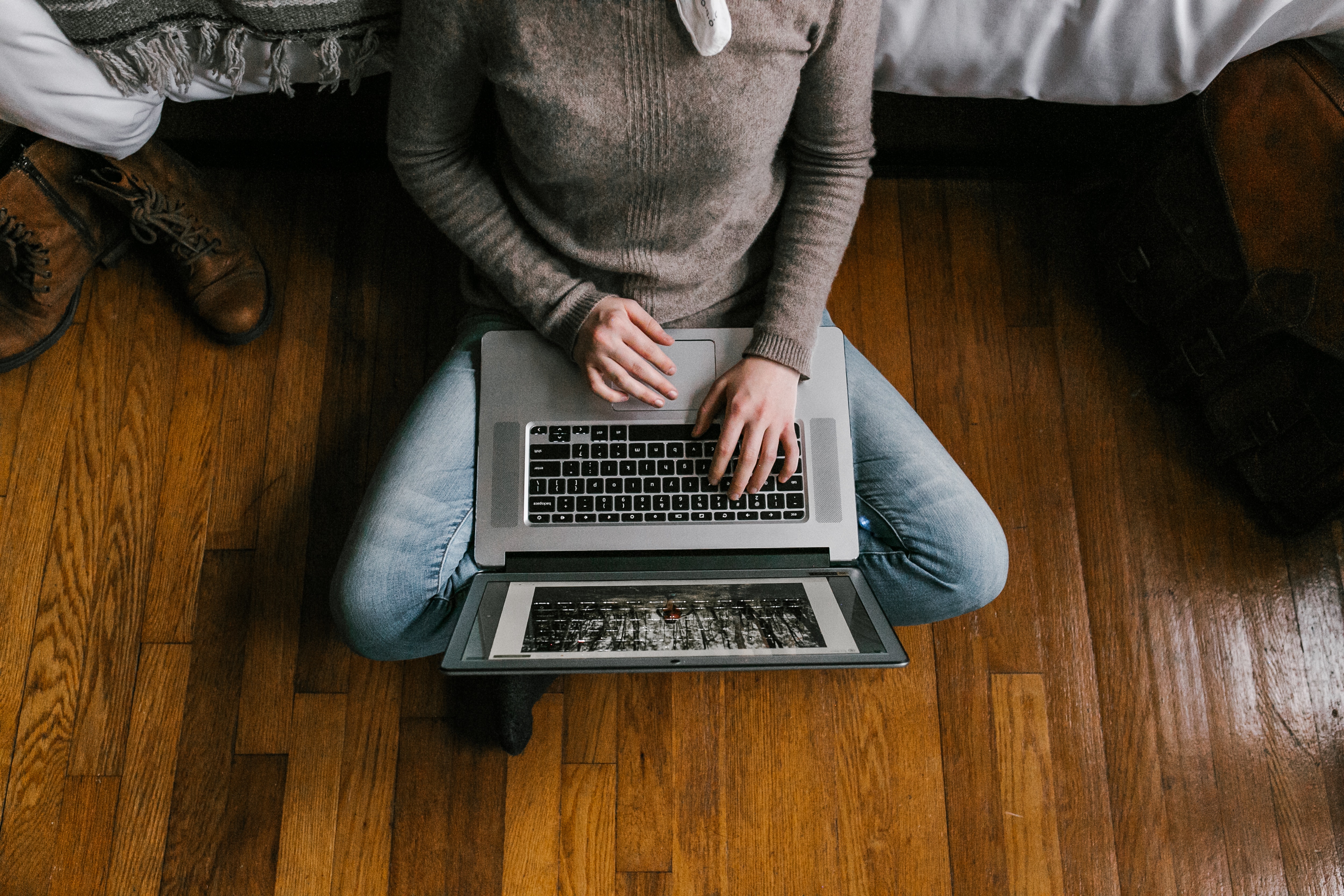 Person sitting on hardwood floor working on a laptop.