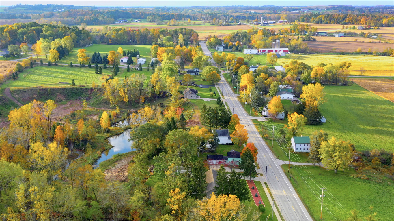 rural landscape with street dividing home plots with greenery, trees, and smaller homes on both sides
