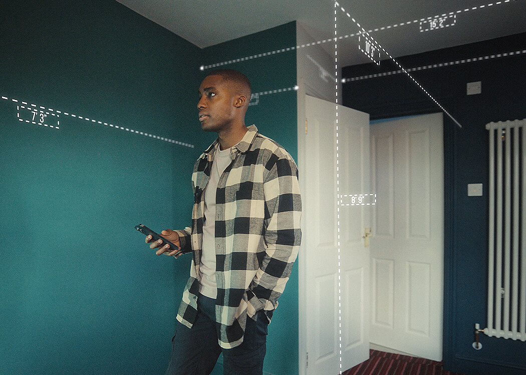 Male in home measuring his room's dimensions with his mobile device. 