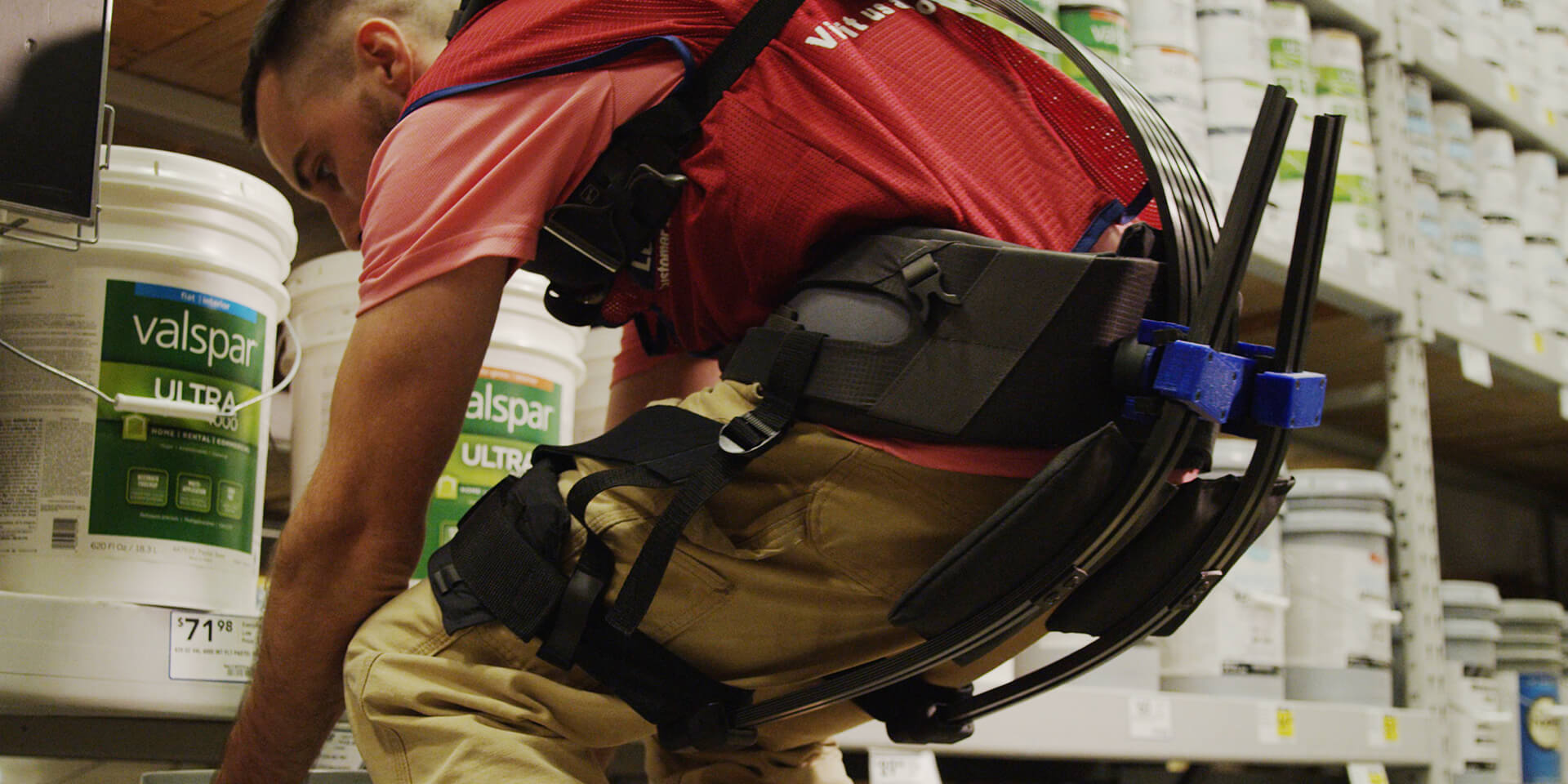 Lowes Home Improvement associate on sales floor lifting heavy object while wearing soft robotic exoskeleton for assistance.