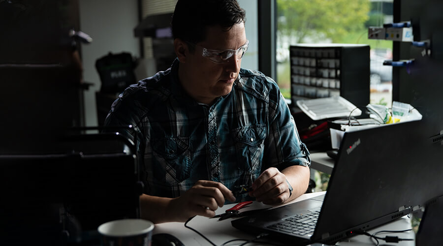 Male Lowe's Innovation Labs team member working on laptop and checking circuitry. 