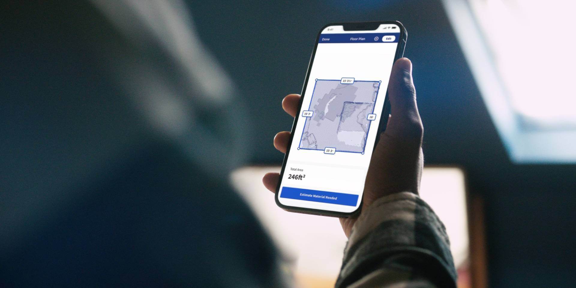Hand holding a mobile device displaying room dimensions taken with the Measure Your Space experience. 